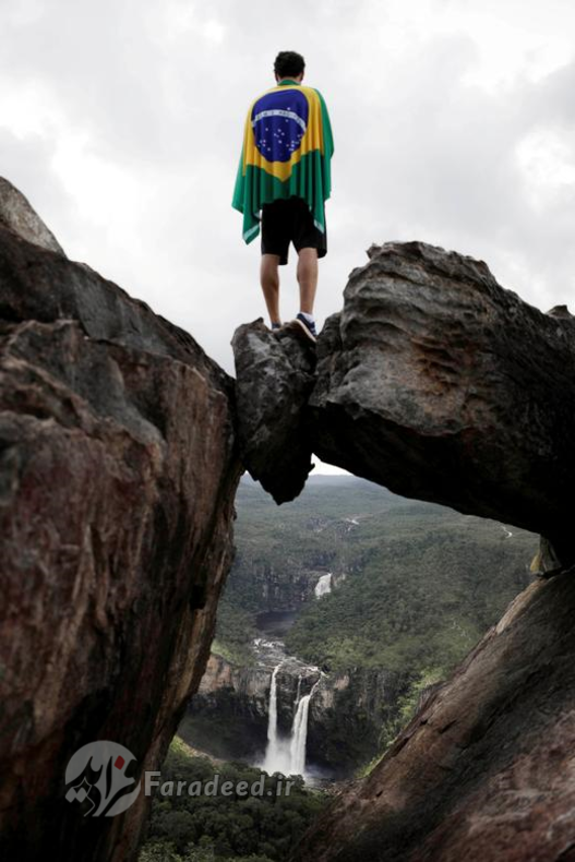 گردشگری با پرچم برزیل بروی شانه هایش بر فراز یک صخره در The Leap from Garimpo ایستاده است. برزیل، 17 مارس، 2018.